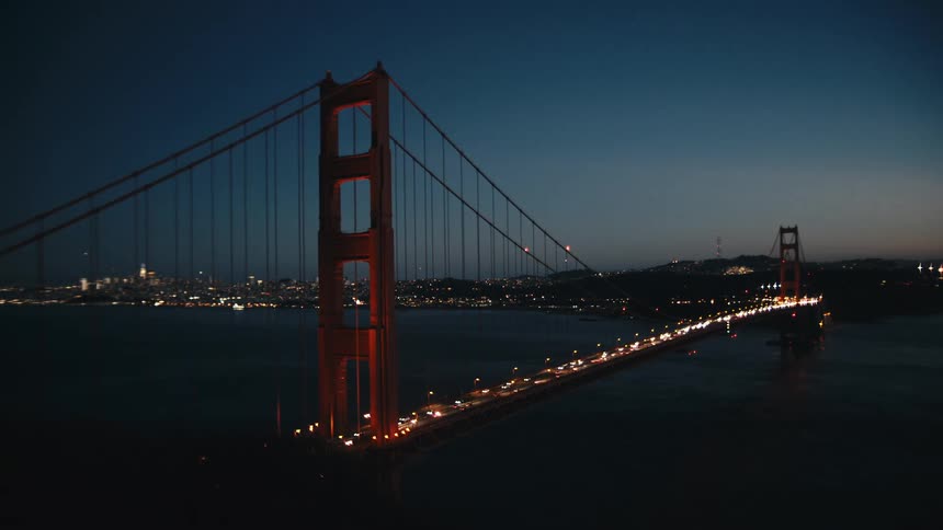 A cable bridge at night is busy with cars moving in and out of the city