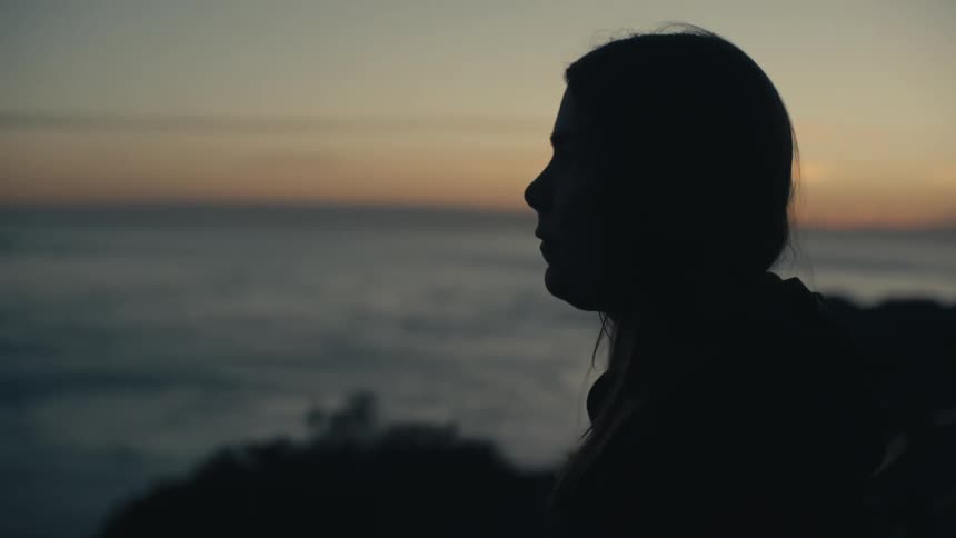 A woman is standing on the shoreline staring out over the ocean at sunset