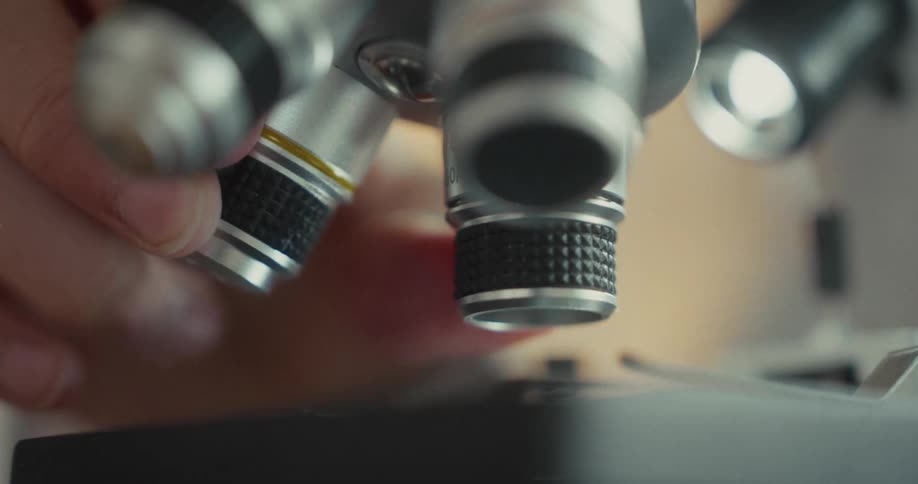 A hand is adjusting the microscope lens in a lab