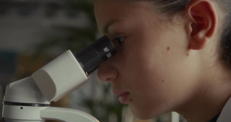 Woman in an indoor space looking closer at a microscope