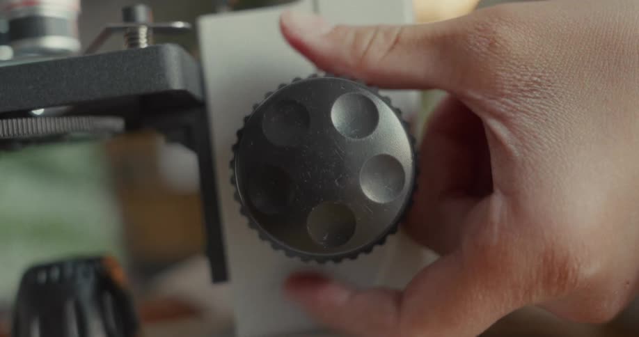 A person turns the dial on the microscope