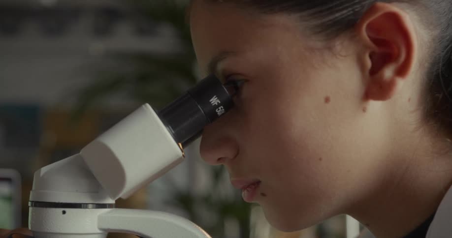 Woman in white coat looking into a microscope