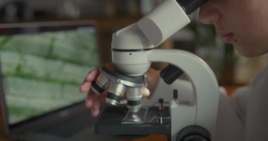 A girl turns the lens on the microscope while sitting in the lab