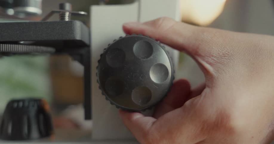 Hand rotating a black piece of a microscope stand