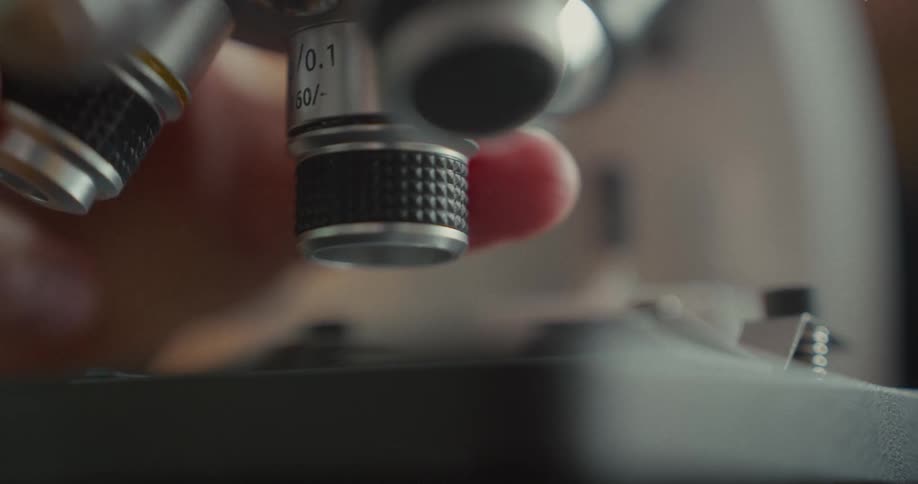 A persons hand is switching lenses on a microscope in the lab at midday