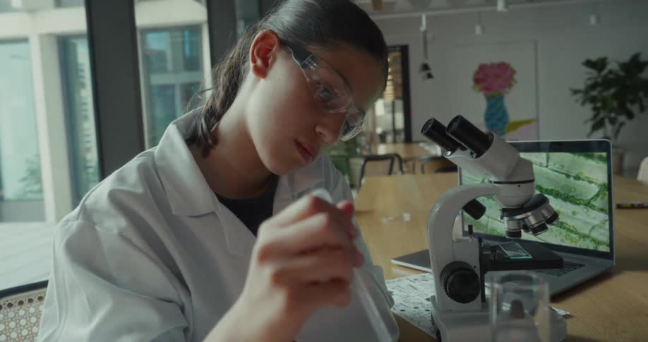 Woman in lab coat handling laboratory instruments with an open laptop in the background