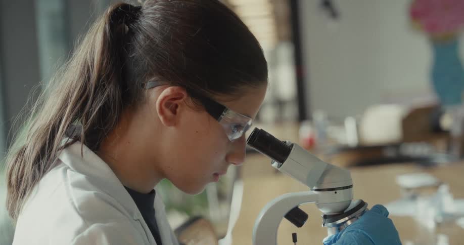 The girl is working in the lab with a microscope