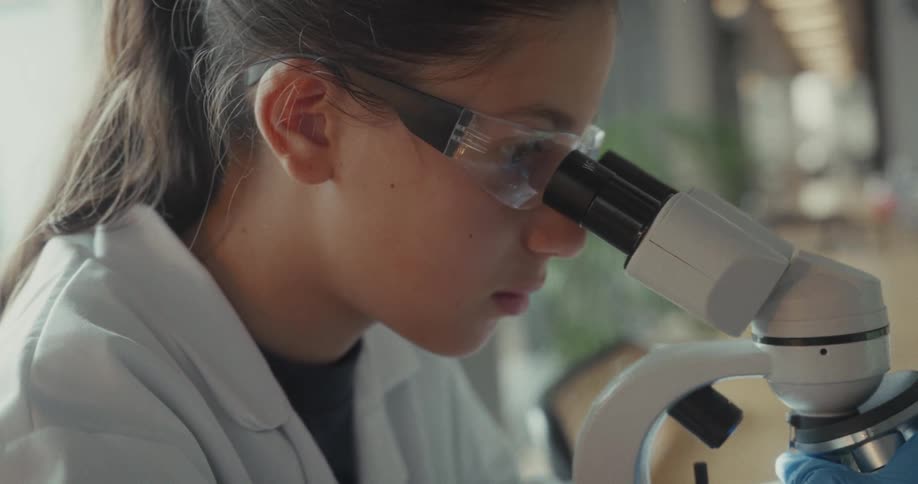 The girl uses a microscope to and adjusts it