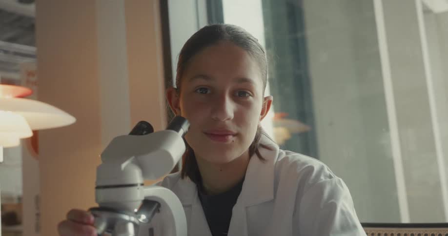 The girl in the lab smiles by the microscope