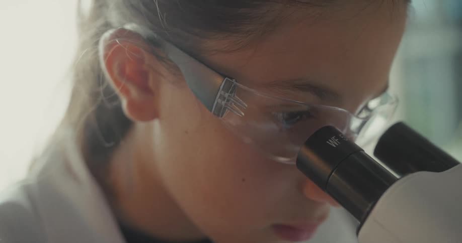 The girl is viewing something in the microscope lens