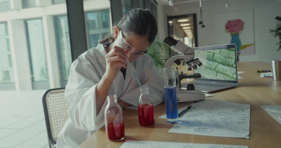 A medical lab assistant is testing a liquid in a tube with a microscope and a laptop beside them