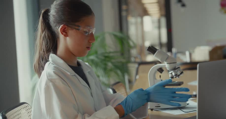 Woman putting on disposable gloves while standing at a table with a microscope