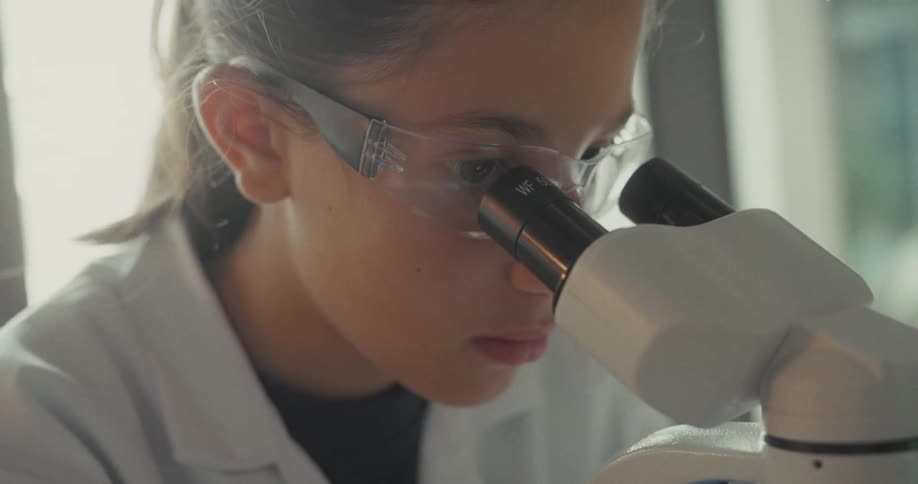 Teenager with lab glasses interacting with microscope