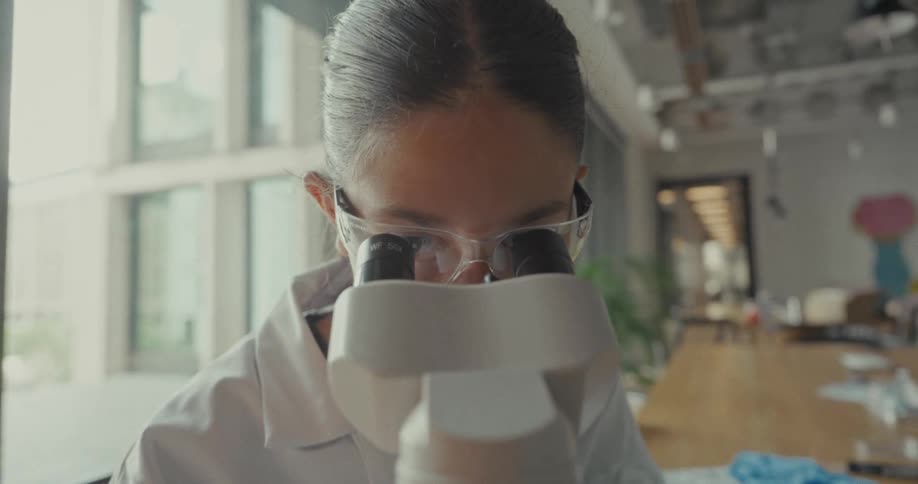 Close up of a female scientist looking through a microscope lens in a lab during daytime