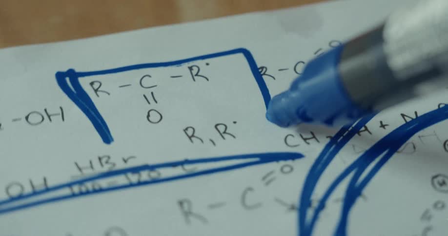 Blue pen scribbling a chemical formula written on a white sheet