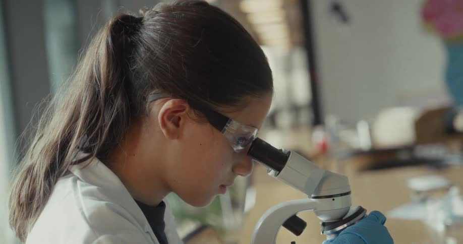 Close up of a young female scientist viewing a sample through a microscopes eye lens in a lab during daytime