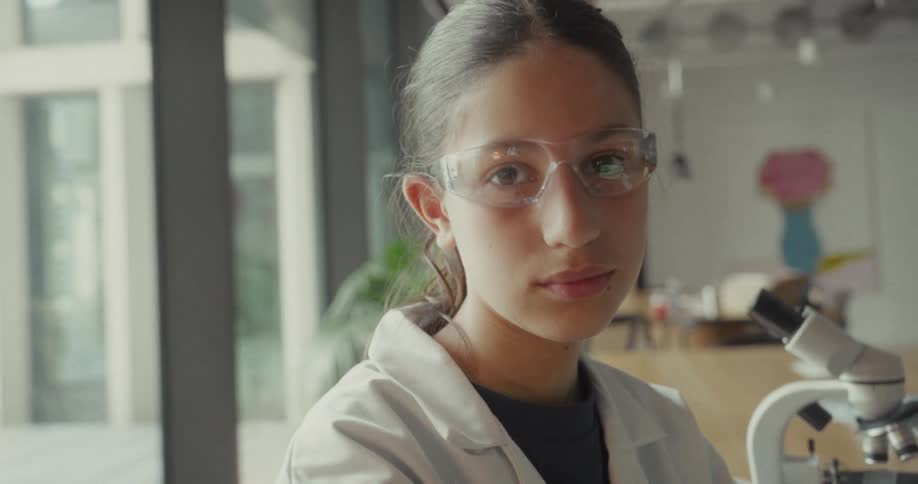 Teenager in a white lab coat putting on lab goggles