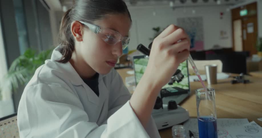 Teenager in white lab coat using a laboratory test tube with blue liquid