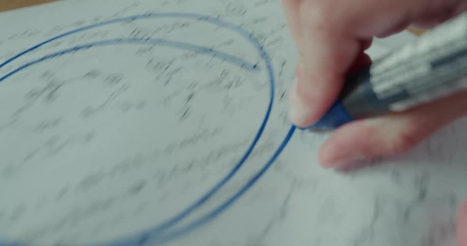 Hand with a blue pen making a circle on a paper with writing