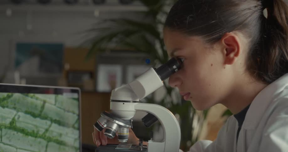 The girl leans to look into the microscope