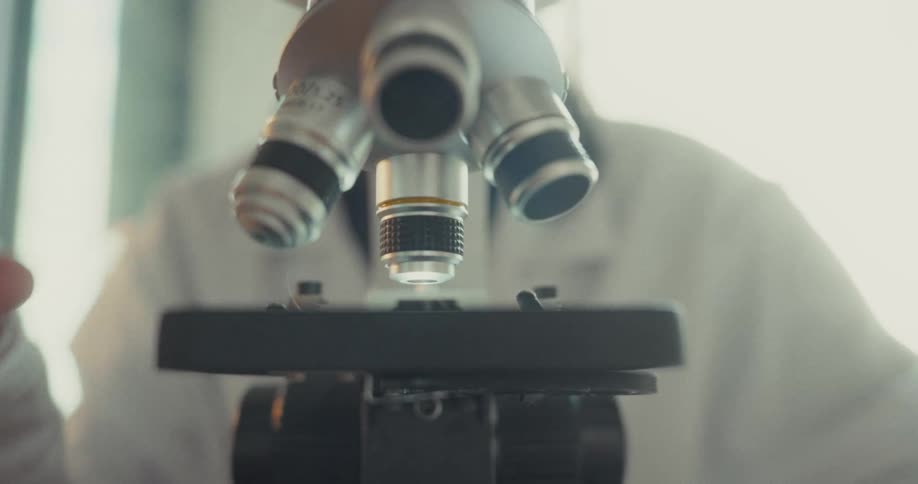 Close up of a young scientist adjusting the objective lens on a microscope in a lab