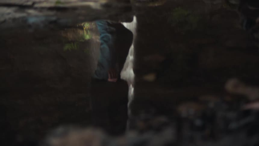 Closeup of a puddle of water reflecting a waterfall and a person walking