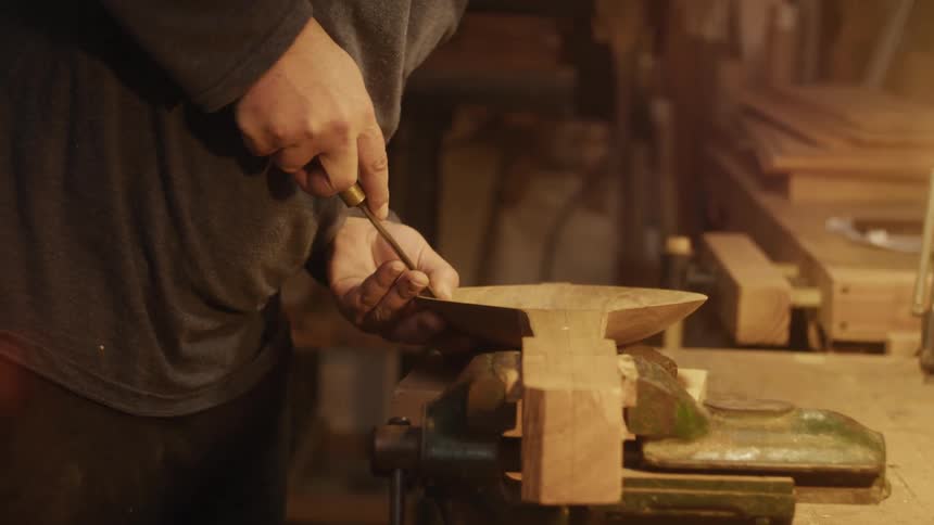 Person carving a wooden container in a lowlight environment