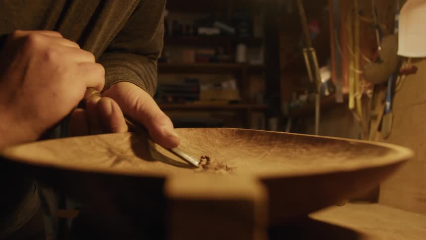 Person with a tool carving a wooden container