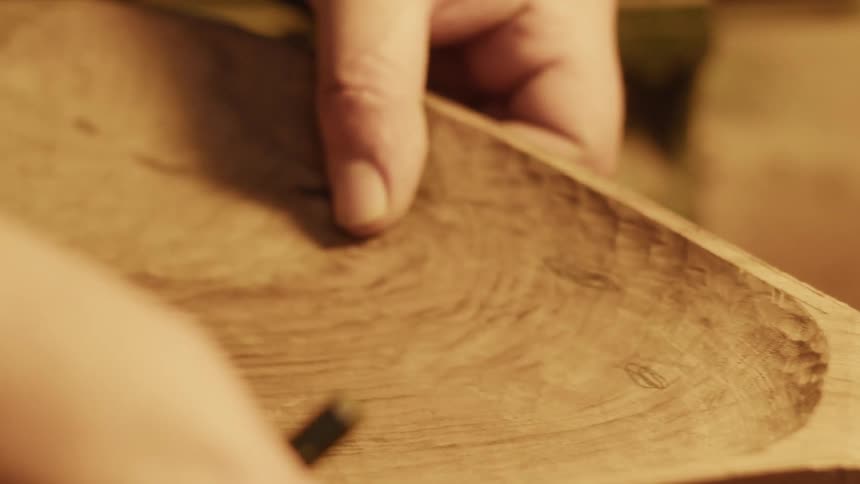 A craftsman is building a wooden tool using a pencil to mark specific points on it