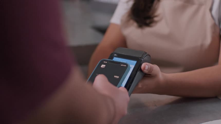 A person holds a smartphone near a card reader to make a contactless payment