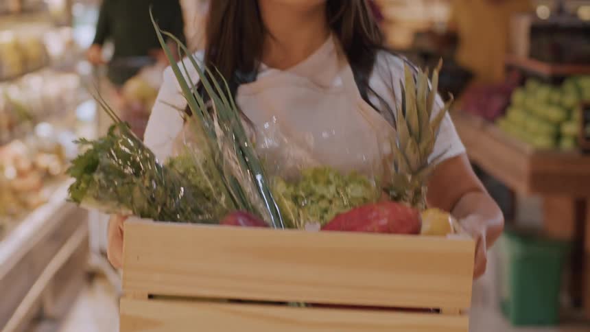 Woman carries a crate of vegetables in a grocery store
