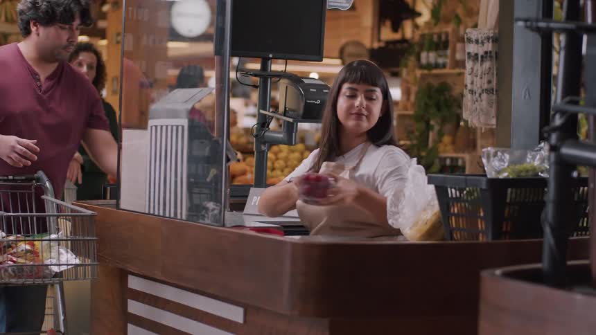 A cashier scans items while a customer places groceries on the counter in a brightly lit supermarket