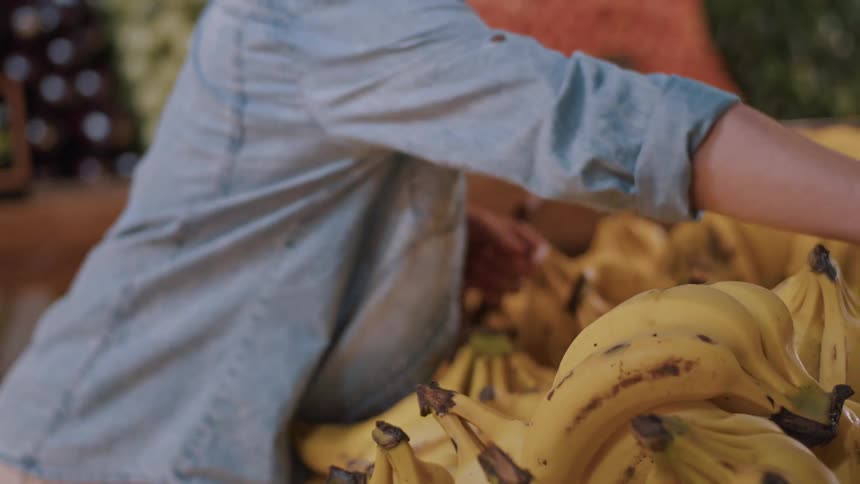 A woman examines a bunch of bananas at a fruit stand