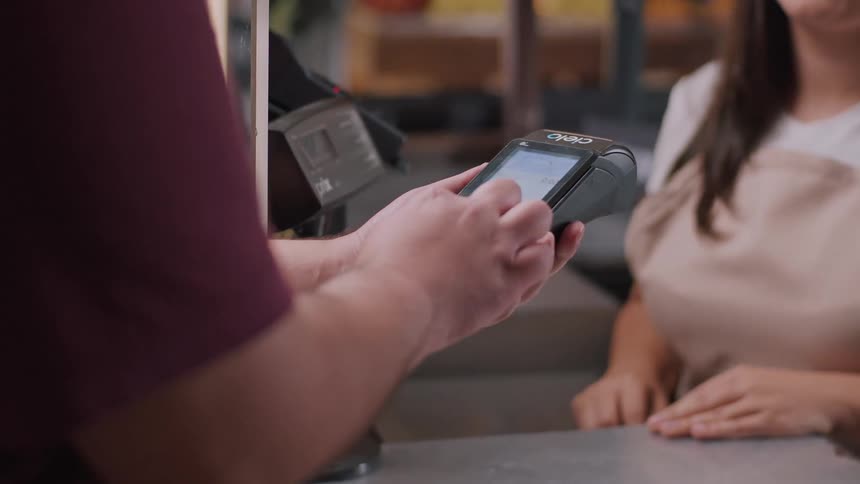 The video shows a transaction taking place at a checkout counter a person is seen attempting to insert a credit card into a payment terminal held by an employee wearing an apron the employee then takes the terminal back and the person holding the card