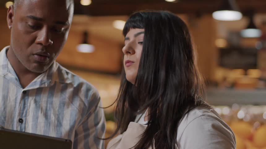 Man with a tablet talking to a woman in a grocery store inside a market