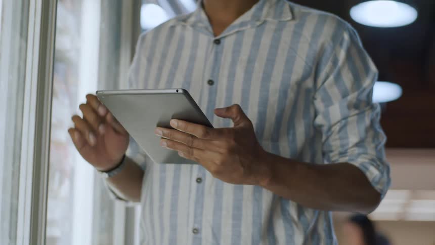 The video shows a man in a striped shirt holding and looking at a tablet in what appears to be a grocery store or retail environment he is standing in front of a refrigerated display case and seems to be using the tablet for inventory management