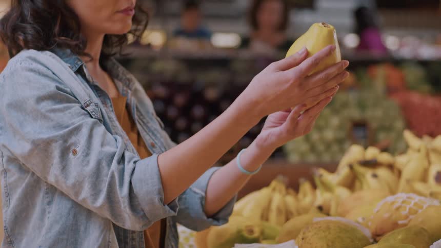 A woman selects a pear while shopping in the produce section of a grocery store