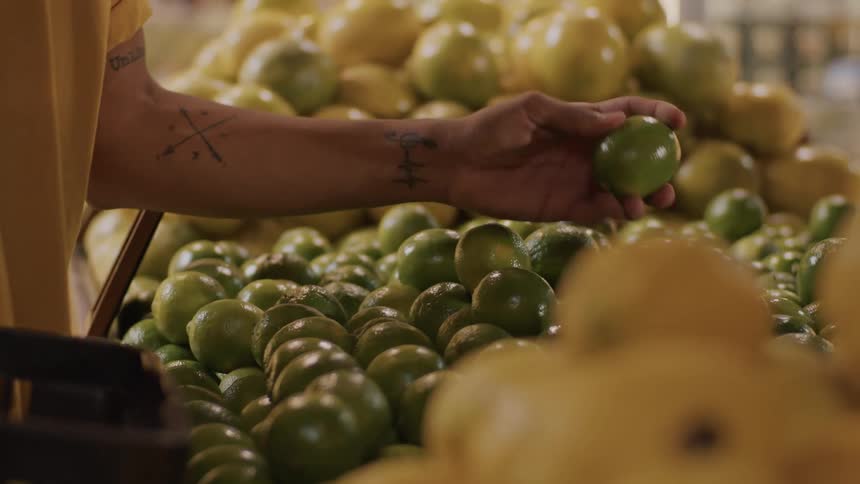 A person selects limes in the produce section of a grocery store