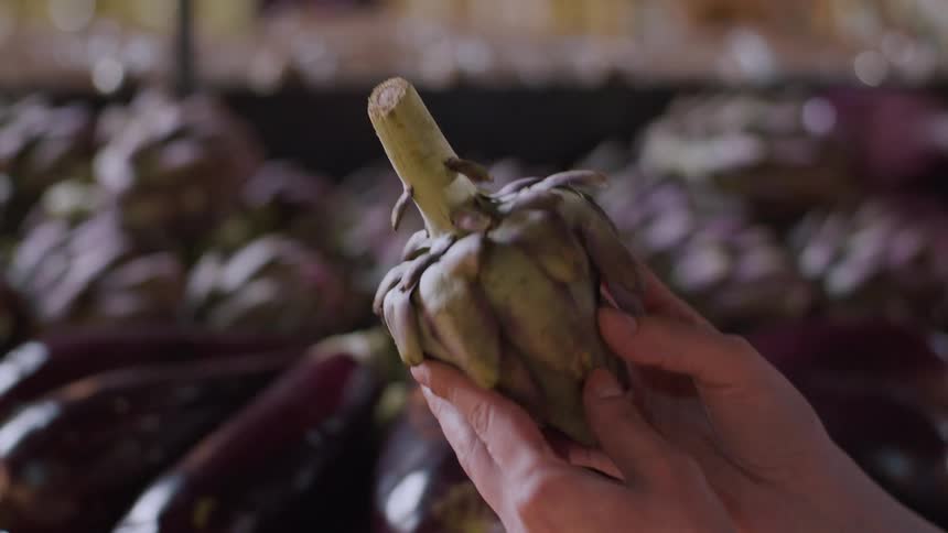 Person holds an artichoke with both hands in a market