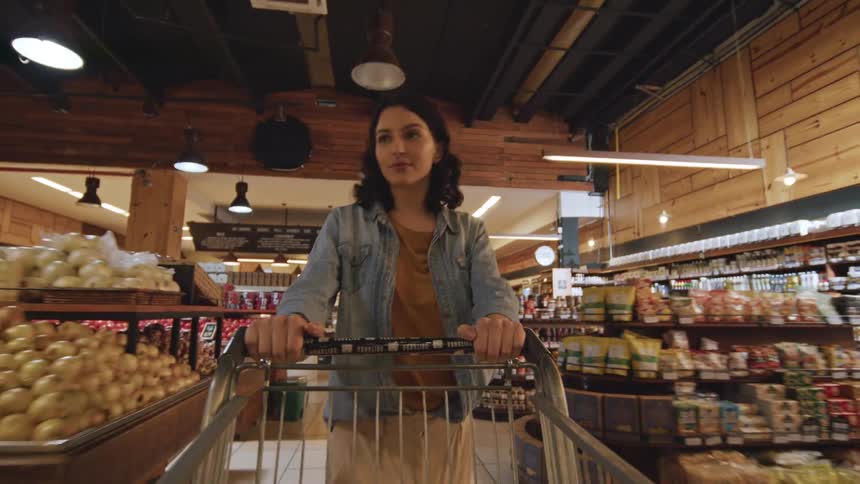 A woman is pushing a shopping cart in a grocery supermarket