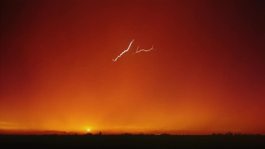 The video shows a dramatic natural phenomenon lightning striking against a vibrant orange and red sunset the sun is visible close to the horizon casting a warm glow across the sky while multiple bright bolts of lightning crisscross