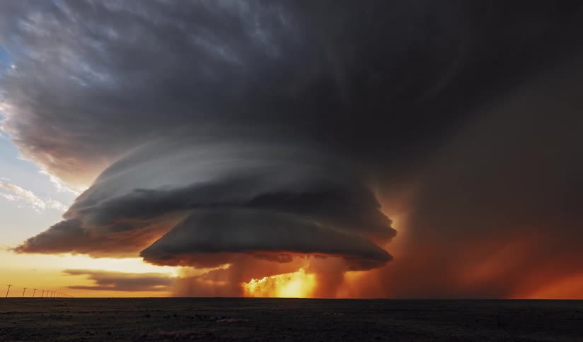 A powerful supercell thunderstorm looms over a wide open plain at sunset