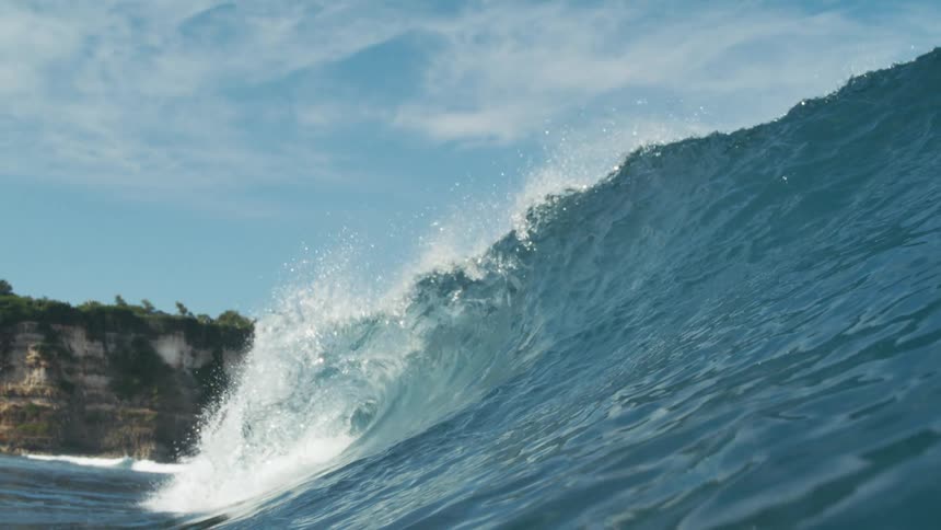 Large wave breaking while it flows towards the coast obscures a seaside cliff on a cloudy day
