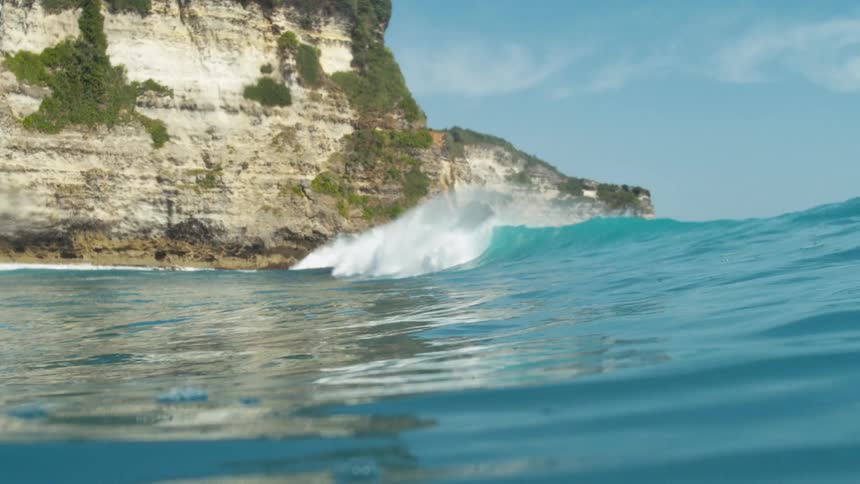 The blue wave crashes against the tall green cliff