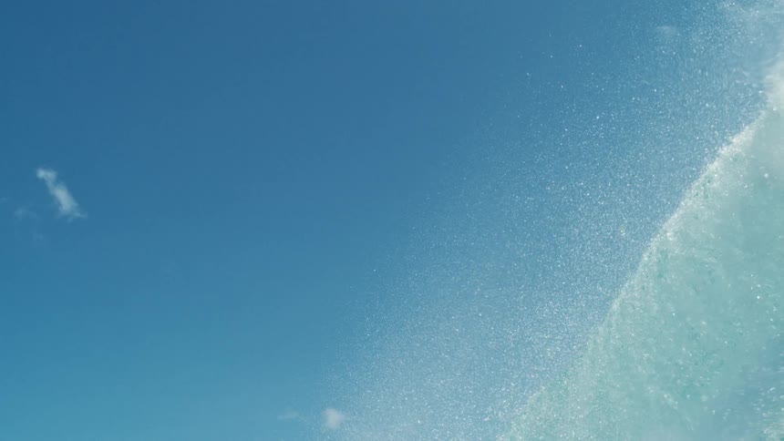 Clear blue wave breaking in the ocean against a clear sky