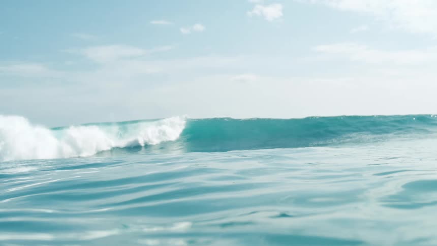 Calm ocean waves move slowly beneath a clear blue sky
