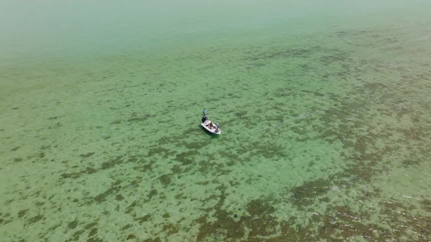 A small boat floats in shallow clear turquoise water over a coral reef