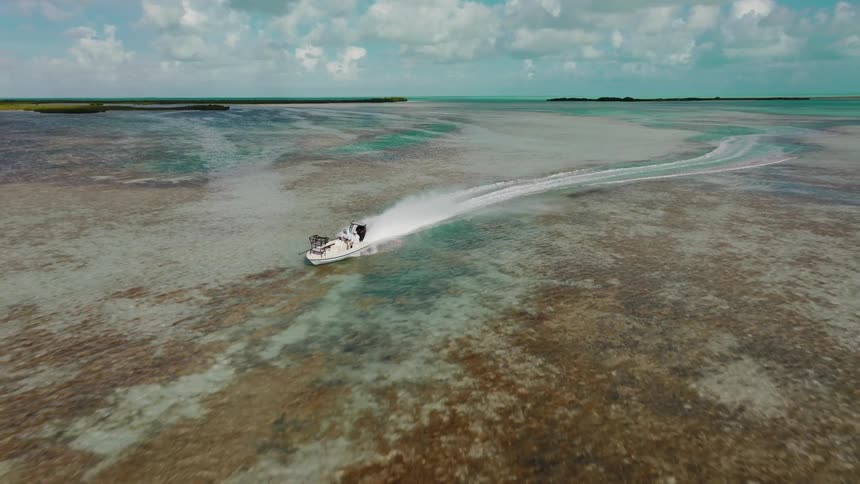 A speedboat speeds through shallow waters leaving a white trail