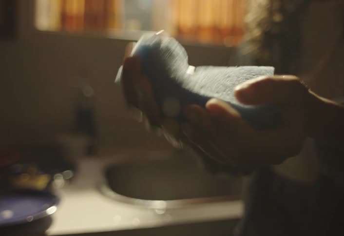 Pair of hands of a person squeezing a sponge and water falling