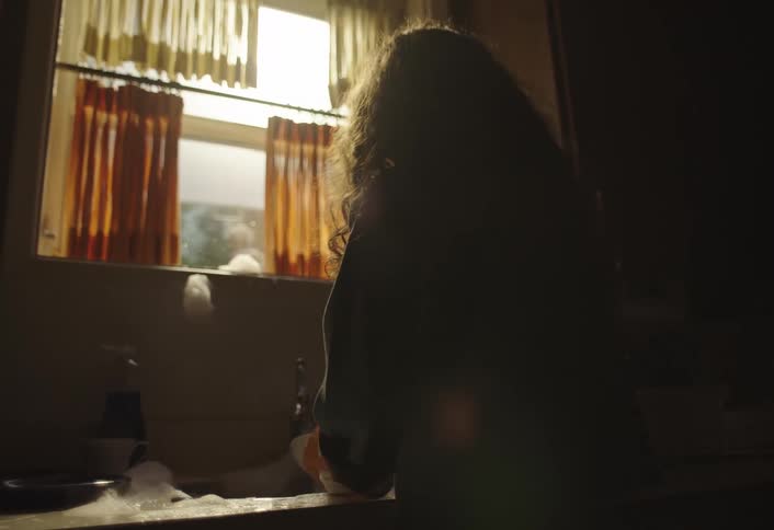 Woman with curly hair washes dishes in the kitchen